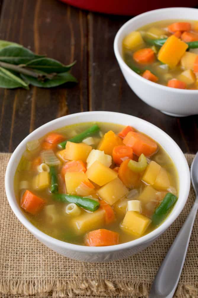 2 white bowls filled with vegetable soup with colors of yellow, orange and green