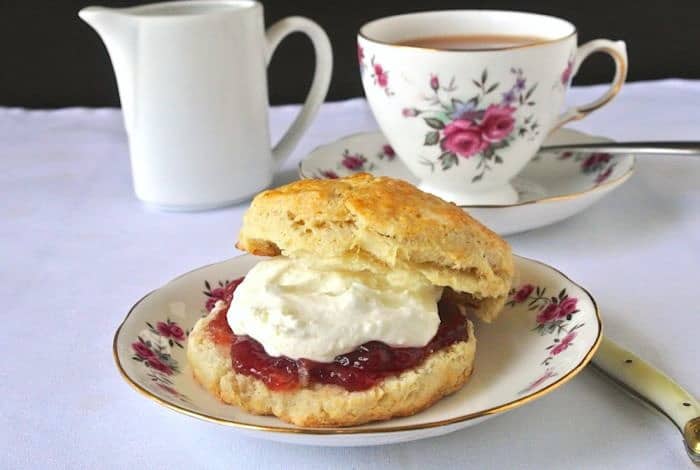 A flowered plate with a scone, jam and clotted cream and a cup of tea in the background