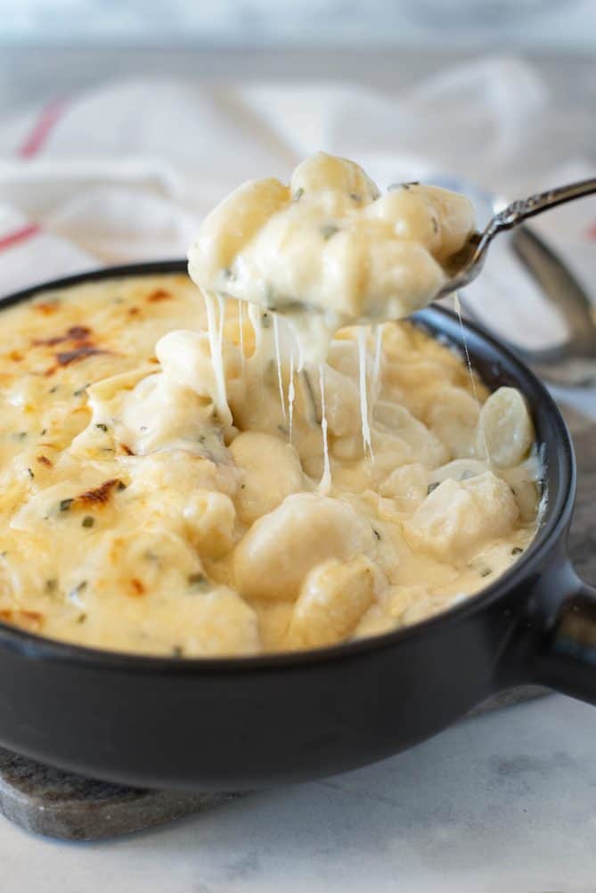 Lifting a spoonful of gnocchi from a cheese sauce with lots of cheese strings