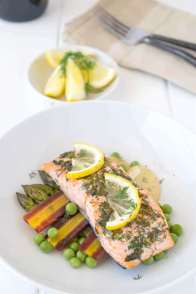 Baked salmon with spring vegetables served on a white plate with fresh lemon slices