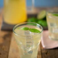 A glass of basil ginger lime tea with ice cubes and basil leaves