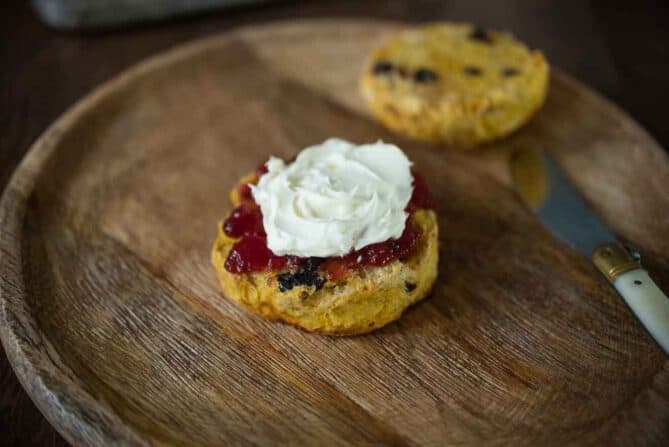 A scone cut in half topped with jam and cream