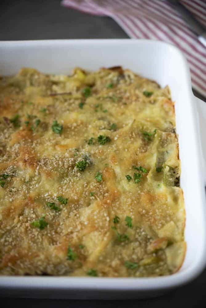 A closeup of baked leeks in a cheese sauce in a white baking dish