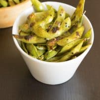 An angled white bowl filled with charred edamame