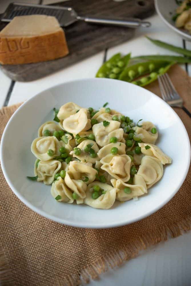 Fresh peas mixed with cheese tortellini in a white bowl with Parmesan cheese