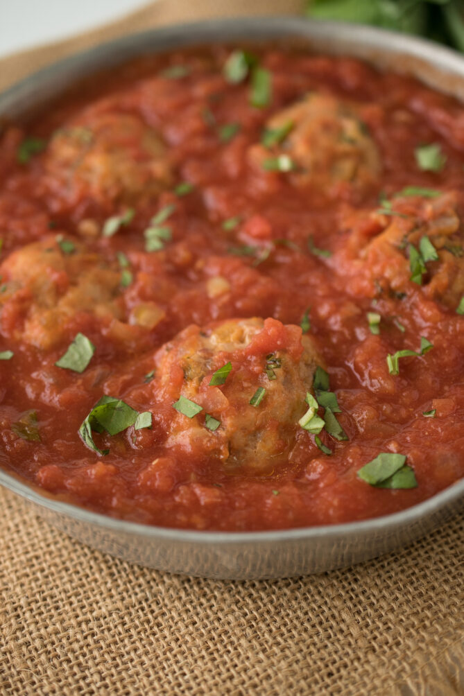 A closeup of a chicken meatball sprinkled with chopped basil