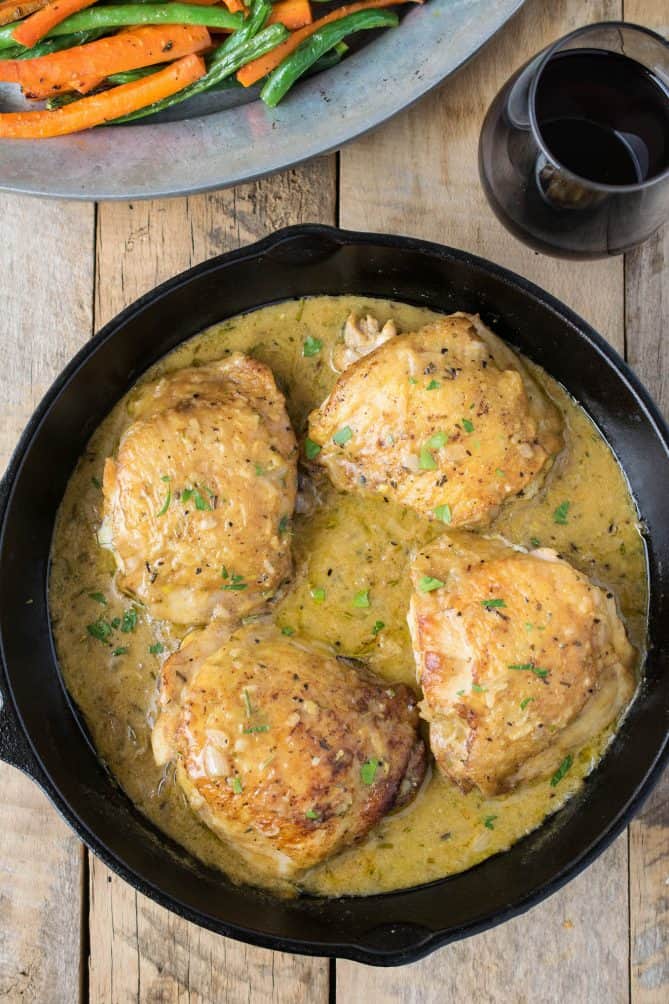 An overhead view of skillet Dijon chicken with vegetables and red wine