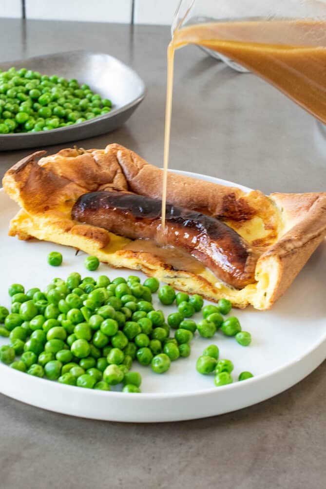 Pouring onion gravy over toad in the hole sausage