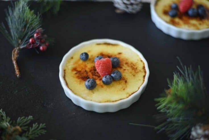 A ramekin filled with eggnog creme brûlée, raspberry and blueberries