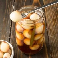 A pickled onion on a fork resting on a jar of English pickled onions