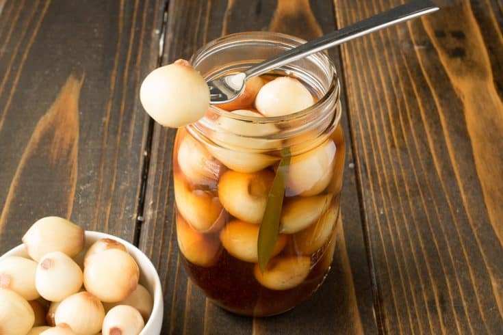 A pickled onion on a fork resting on a jar of English pickled onions
