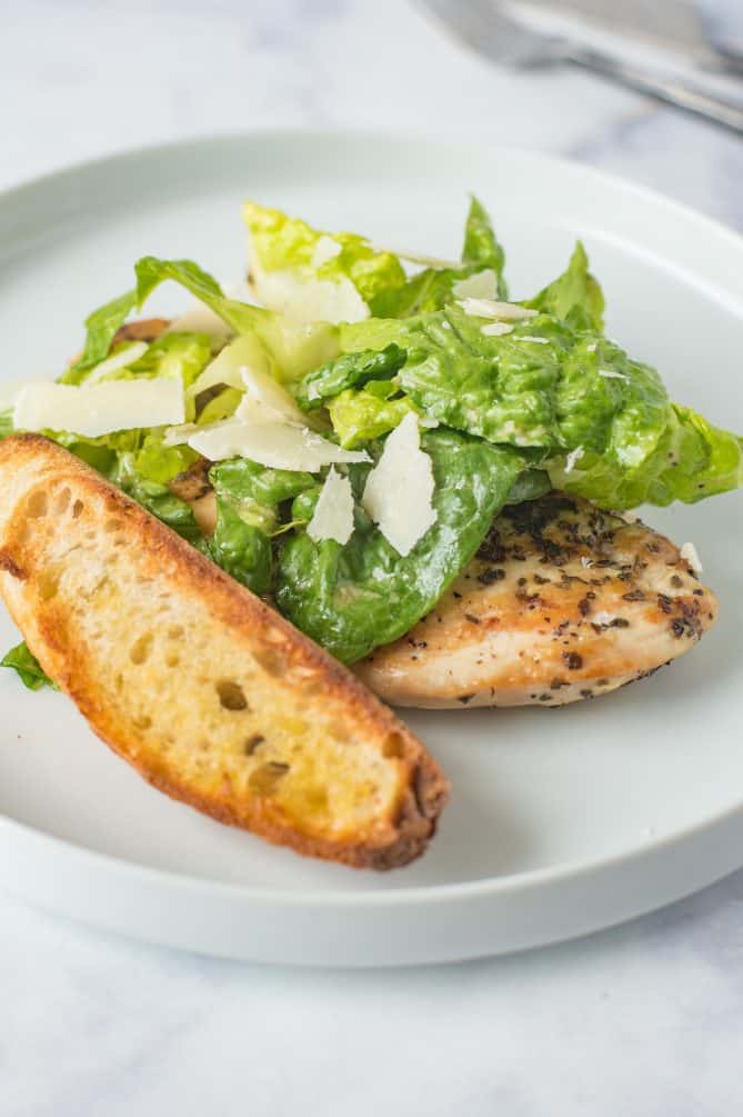 A large crouton with Caesar salad and a chicken breast on a white plate