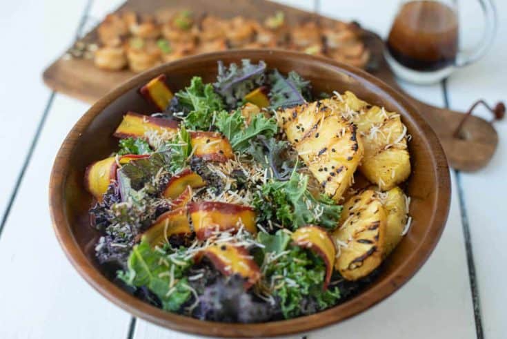 Slices of grilled pineapple on a bed of kale with shaved carrot and toasted coconut
