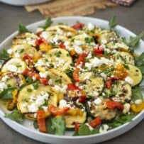 Zucchini and yellow squash on a white round platter with arugula peppers and feta