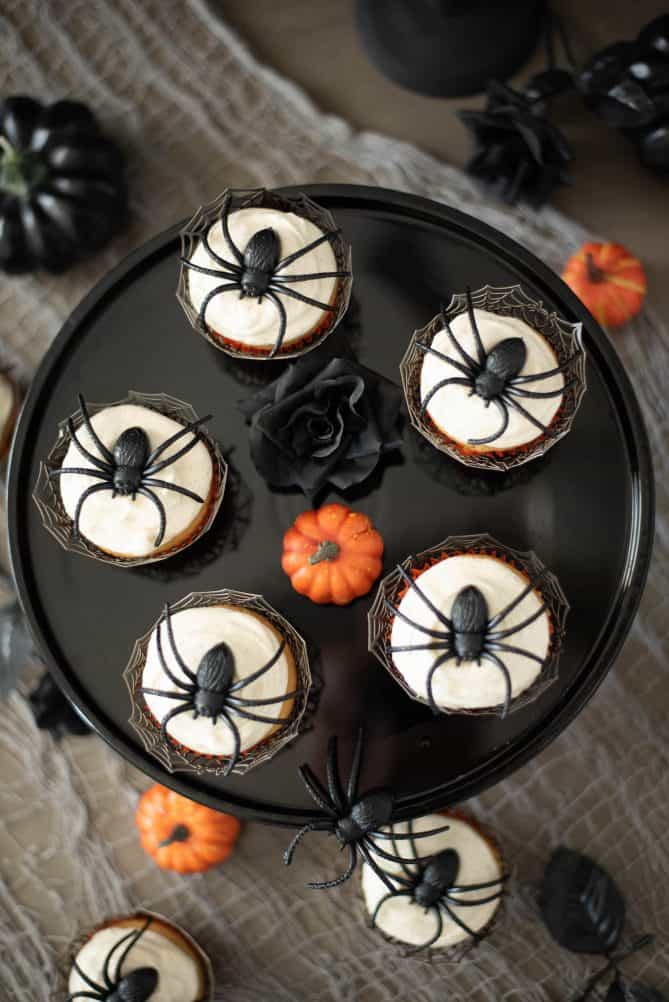 Plastic spiders on top of cupcakes viewed from overhead with black roses and a mini pumpkin