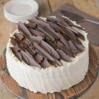 A buttercream frosted chocolate cake topped with chocolate shards on a cake stand