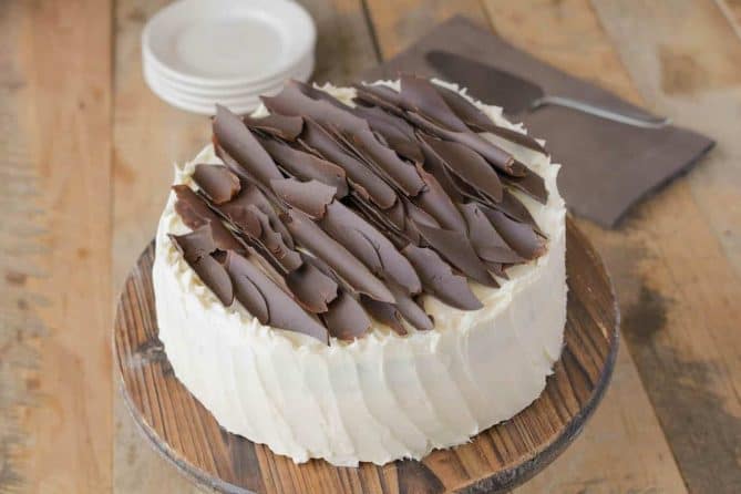 A buttercream frosted chocolate cake topped with chocolate shards on a cake stand