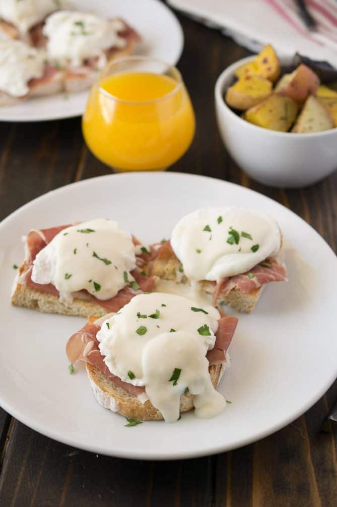 3 Italian eggs Benedict on a plate with a glass of orange juice and potatoes