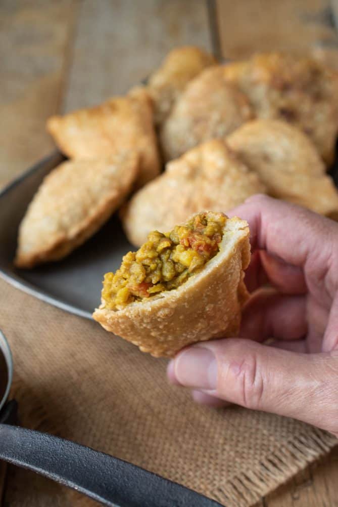 Holding a lentil samosa cut in half showing the filling