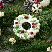 A peppermint cookie decorated with white icing, green leaves and pomegranate seeds