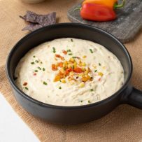 The dip in a black bowl garnished with corn, peppers and green chives