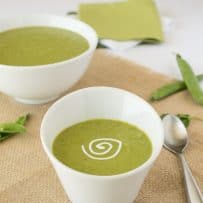 An angled white bowl of pea soup with a sour cream swirl