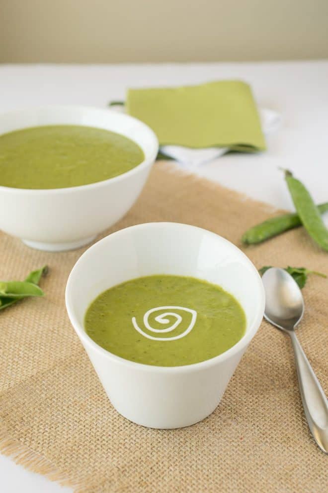 An angled white bowl of pea soup with a sour cream swirl