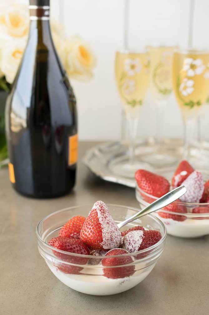 A side view of a glass bowl of whole strawberries with fresh cream with a spoon