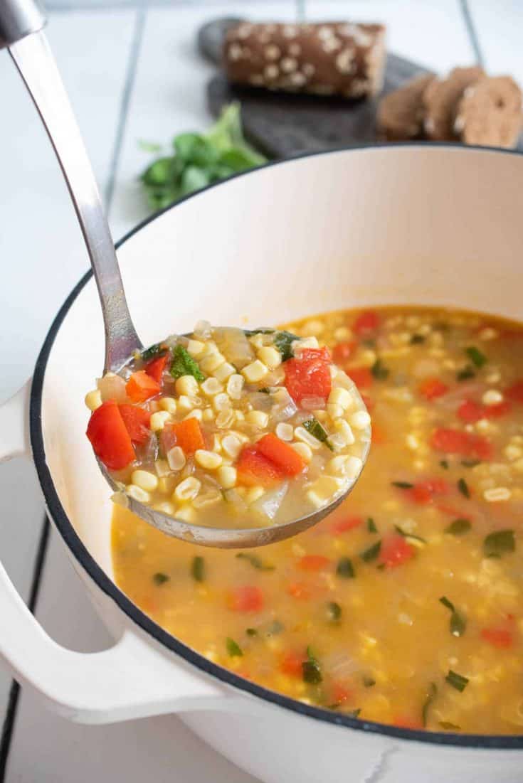 A ladle full of corn and vegetable soup