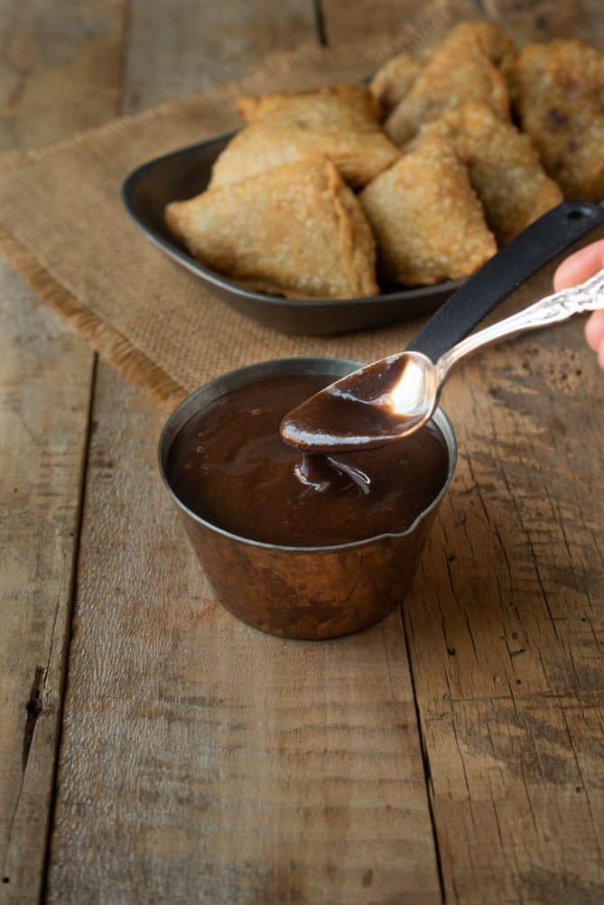 Getting a spoonful of tamarind and date chutney out of a small container