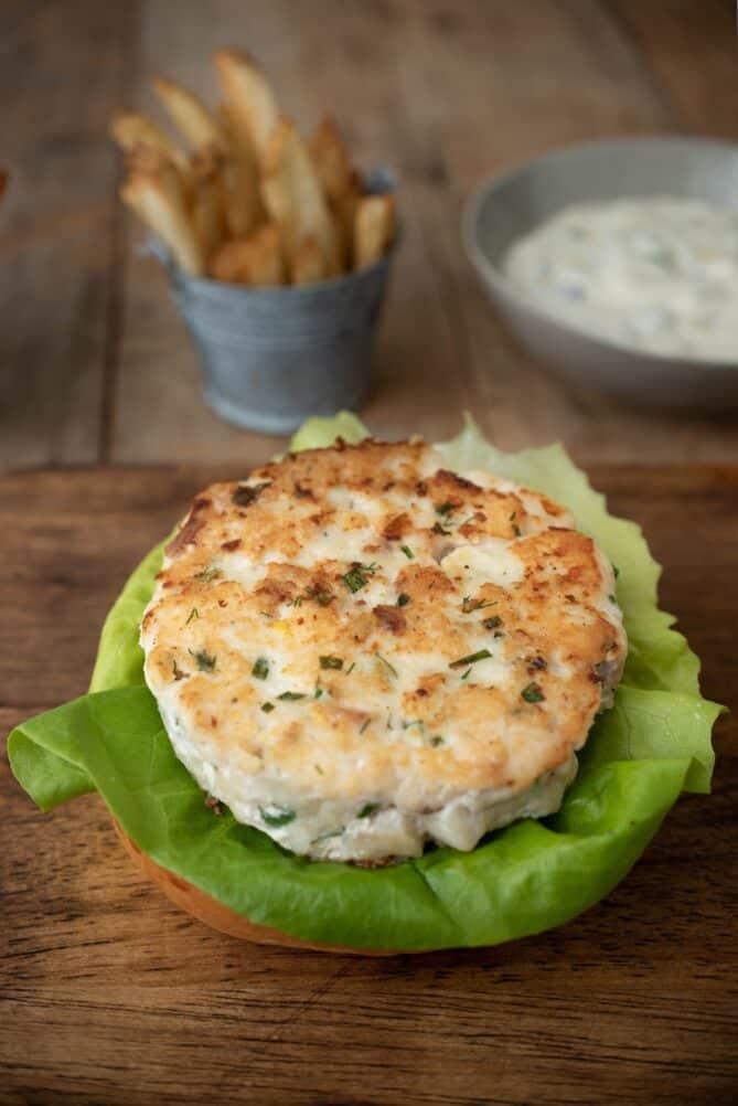 A cooked fish burger on a bed of lettuce and a bun