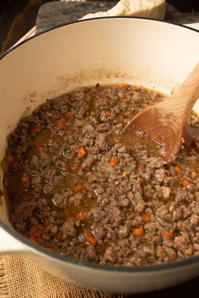 Ground beef and Italian sausage with carrots made into a Bolognese sauce without tomato in a pan with a wooden spoon