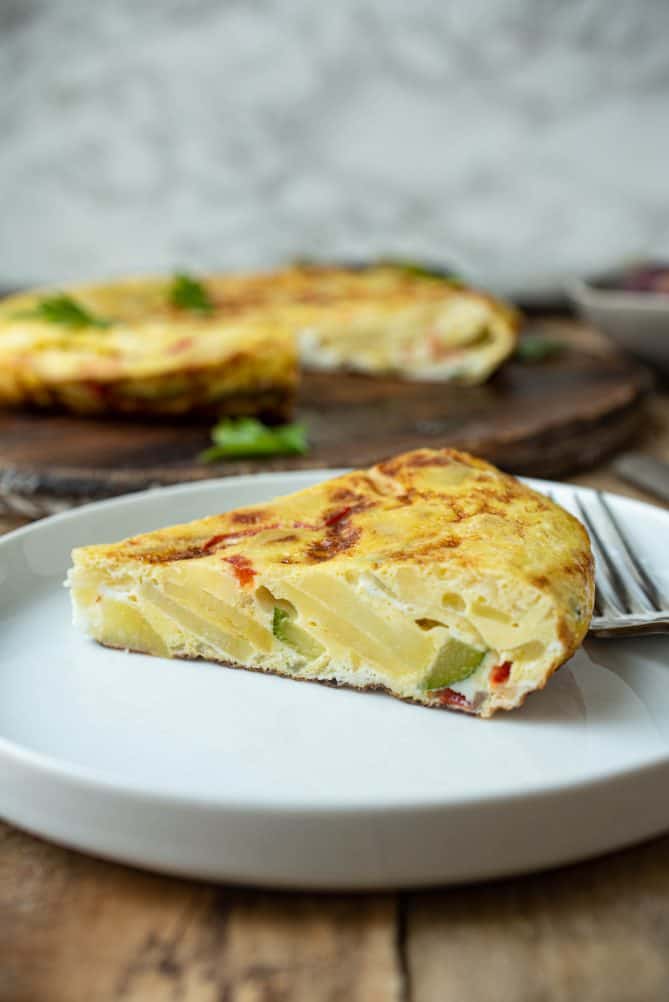 A slice of Spanish omelette on a plate viewed from the side showing the colorful vegetables inside