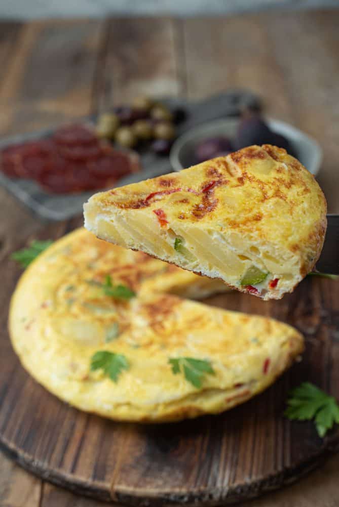Lifting a slice of Spanish tortilla showing the potato slices, red pepper and green zucchini/courgette on the inside