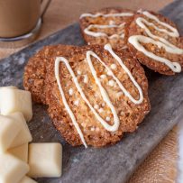 4 white chocolate Florentine cookies on a grey serving board with squares of white chocolate